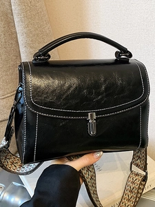 Fashionable black faux leather handbag with white contrast stitching and a wide woven strap