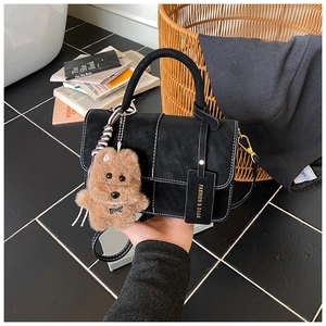 Detail of black matte handbag with contrast stitching and plush dog charm pendant