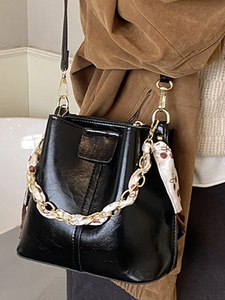 Minimalist black patent leather bucket bag with gold chain and silk scarf handle