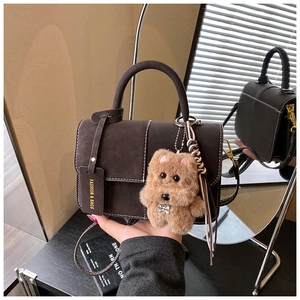 Detail of dark brown suede handbag with white stitching and plush puppy pendant