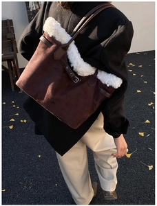 Detail of a brown suede tote bag with white plush trim and leather shoulder strap accents