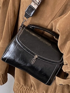 Chic black glossy leather shoulder bag with white contrast stitching and a wide jacquard strap