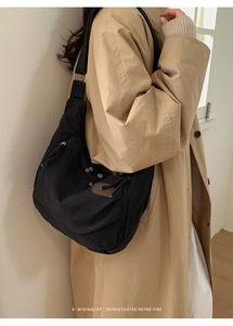 Minimalist black nylon dumpling bag worn over a beige trench coat for a retro vibe