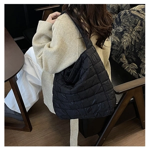 Detailed view of black quilted puffer tote bag on a model in a cozy cafe setting