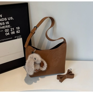 Detail of brown vintage PU leather bag with a plush rabbit charm and adjustable strap