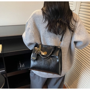 Detail of glossy black leather handbag featuring a golden lock and metallic chain strap