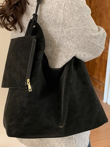 Black matte suede tote bag with matching zippered pouch shown on shoulder in a home setting