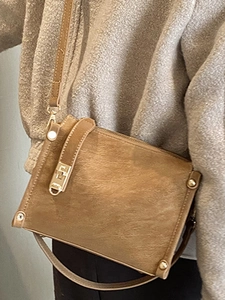 Vintage brown crossbody bag with gold studs and matte texture on a grey coat background