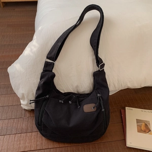 Detail view of the black canvas tote bag with drawstrings and side zippers on wood floor