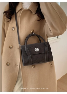 Detail shot of a dark grey retro leather handbag with round metal twist lock and top handle