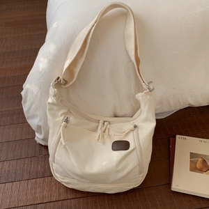 Detail of cream canvas tote bag showing three front zippers and brown leather patch accent