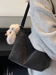 Minimalist black suede shoulder bag with wide leather strap and plush bird charm on a model