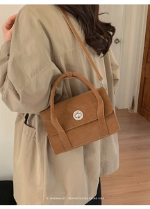 Close-up of caramel brown retro crossbody bag with silver round metal clasp on beige trench coat