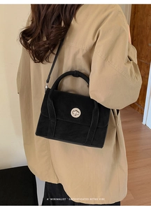 Detail of minimalist retro black suede shoulder bag with circular silver metal twist lock