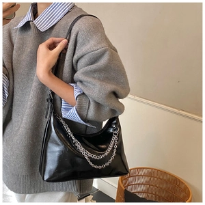 Détail d'un sac hobo en cuir noir brillant orné de chaînes en métal argenté stylées