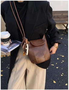 Detail der braunen Vintage-Eimertasche mit Perlenquastenanhänger und Ziernaht-Design