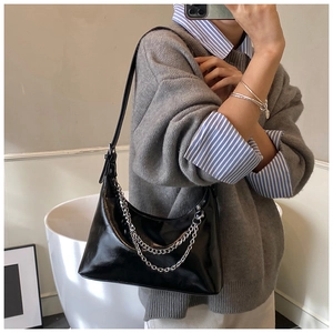 Détail du sac sous l'aisselle noir brillant avec double chaîne argentée et forme demi-lune