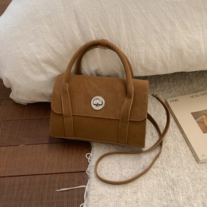 Close-up of brown matte leather bag with silver rotary buckle on a cozy white rug