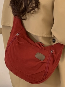 Red canvas hobo tote bag with multi-zipper pockets worn by model in a trench coat
