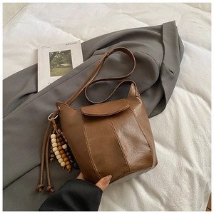 Detail einer braunen matten PU-Leder Beuteltasche mit Holzperlen-Deko und Klappenverschluss