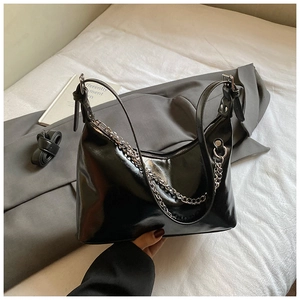 Détail d'un sac hobo en cuir noir brillant avec chaîne argentée et bandoulière longue