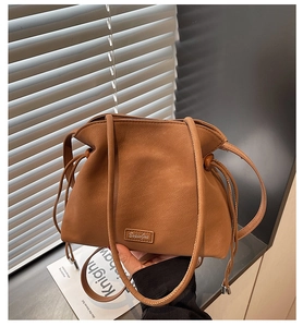 Detail of a brown leather bucket bag showing the drawstring closure and textured finish