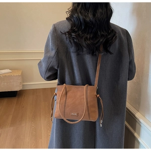 Detail view of brown leather crossbody bag with drawstring side and embossed patch