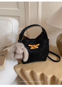 Dettaglio di una borsa a secchiello vintage nera opaca con fibbia dorata e ciondolo a coniglio