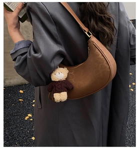 Close-up of brown crescent bag with leopard embossed leather and a cute bear charm