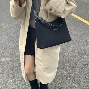 Detail of minimalist black tote bag with silver buckle worn during outdoor city commute