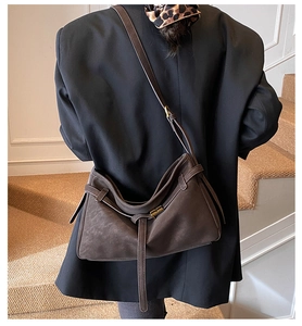 Detail of dark brown suede shoulder bag with adjustable strap and metallic hardware