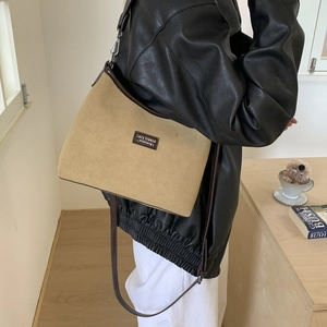 Detail of khaki suede hobo bag with leather trim and logo worn by model in a cozy setting