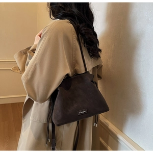 Detail of a dark brown drawstring bucket bag with textured finish and tassel detail