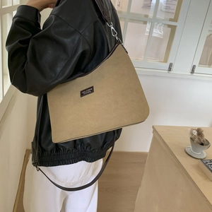 Detailed back view of a khaki suede shoulder bag with brown leather trim on a model