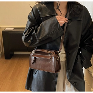 Détail d'un sac oreiller en cuir marron foncé porté avec un élégant manteau noir