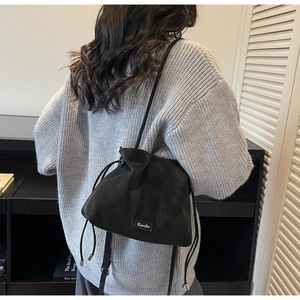 Detail view of a black drawstring bucket bag worn by a model in a modern studio