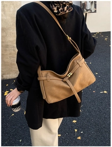 Brown leather tote bag with gold buckle shown on shoulder in autumn street scene