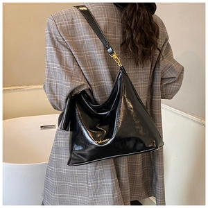 Detail view of black glossy PU leather hobo bag with gold logo on a gray suit model