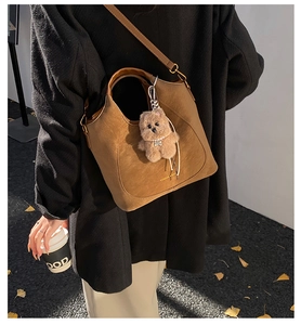 Detail of caramel brown suede tote bag with gold logo and plush bear charm decoration