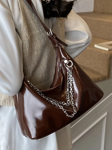 Sac hobo marron foncé brillant avec chaîne argentée porté par un mannequin chic