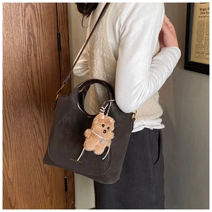 Detail of dark brown faux suede bucket bag with teddy bear charm and gold lettering