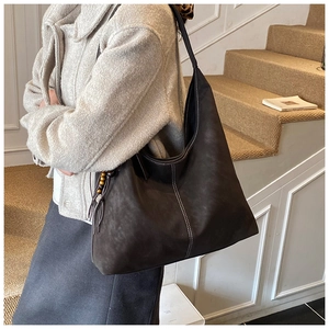 Détail du sac hobo en daim marron avec surpiqûres contrastées et pendentif à pompon en bois