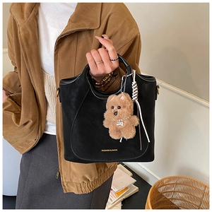 Detail of black tote bag with brown plush bear charm and woven bohemian pendant