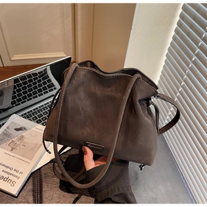 Detail of a soft dark brown suede bucket bag featuring a sleek metal logo on a modern desk