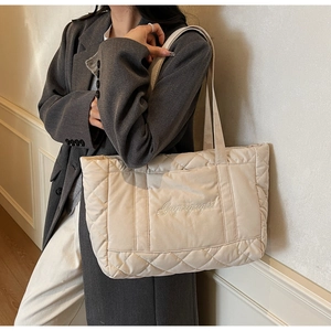 Detail of quilted beige nylon tote bag featuring white cursive embroidery and large capacity