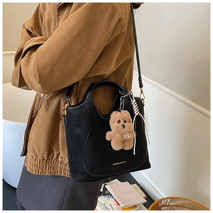 Detail of black matte leather shoulder bag with gold lettering and cute brown plush bear charm