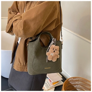 Detail view of dark green matte shoulder bag with golden logo and brown teddy bear charm