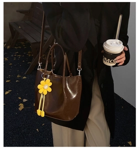 Outdoor lifestyle shot of a large brown tote bag with yellow flower charm and strap