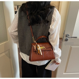 Detail of dark brown polished leather bag with wooden bead charm and metal buckle clasp