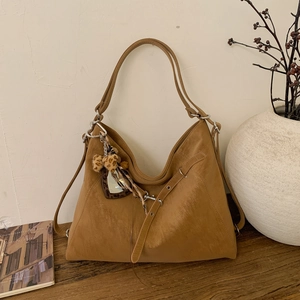 Détail d'un sac Hobo marron avec nœud léopard et breloque cœur sur une table en bois